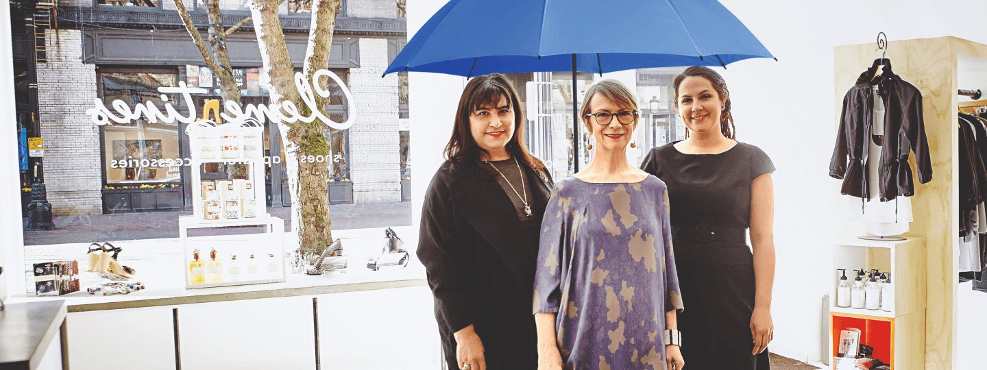 Drei Frauen stehen mit dem blauen Schutzschirm in ihrem Ladengeschäft.