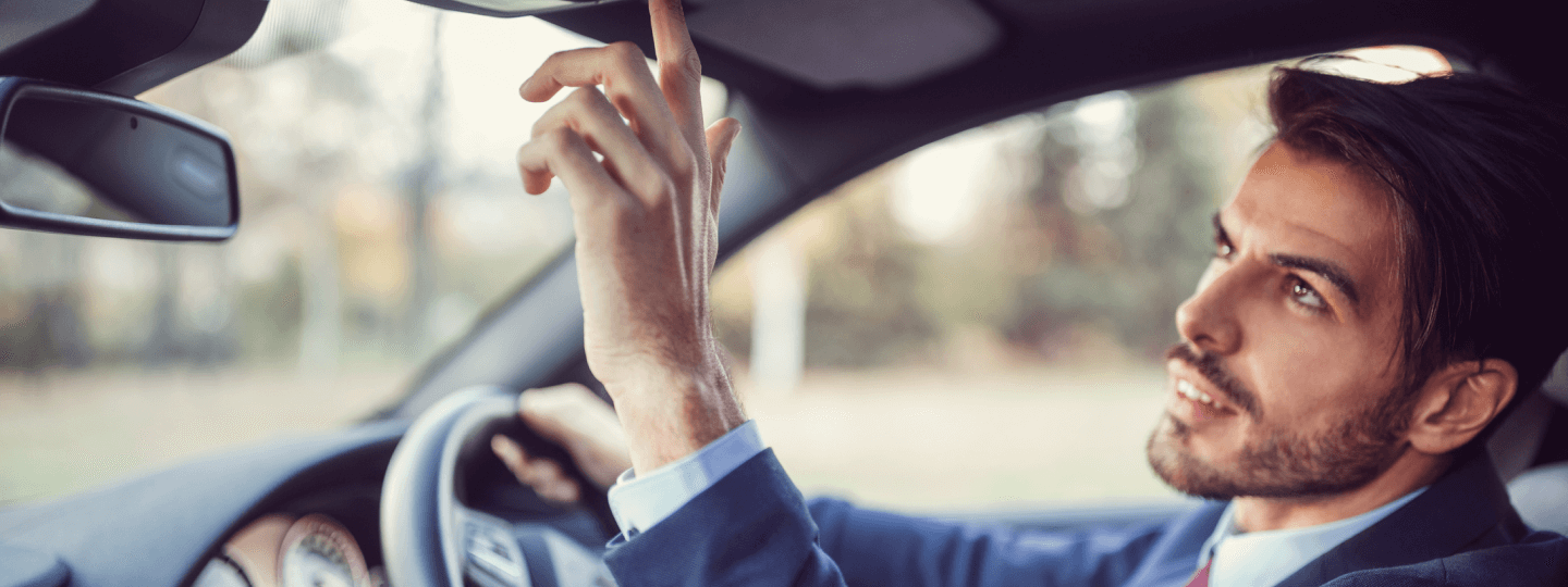 Mann sitzt am Steuer und drückt im Auto einen Knopf.