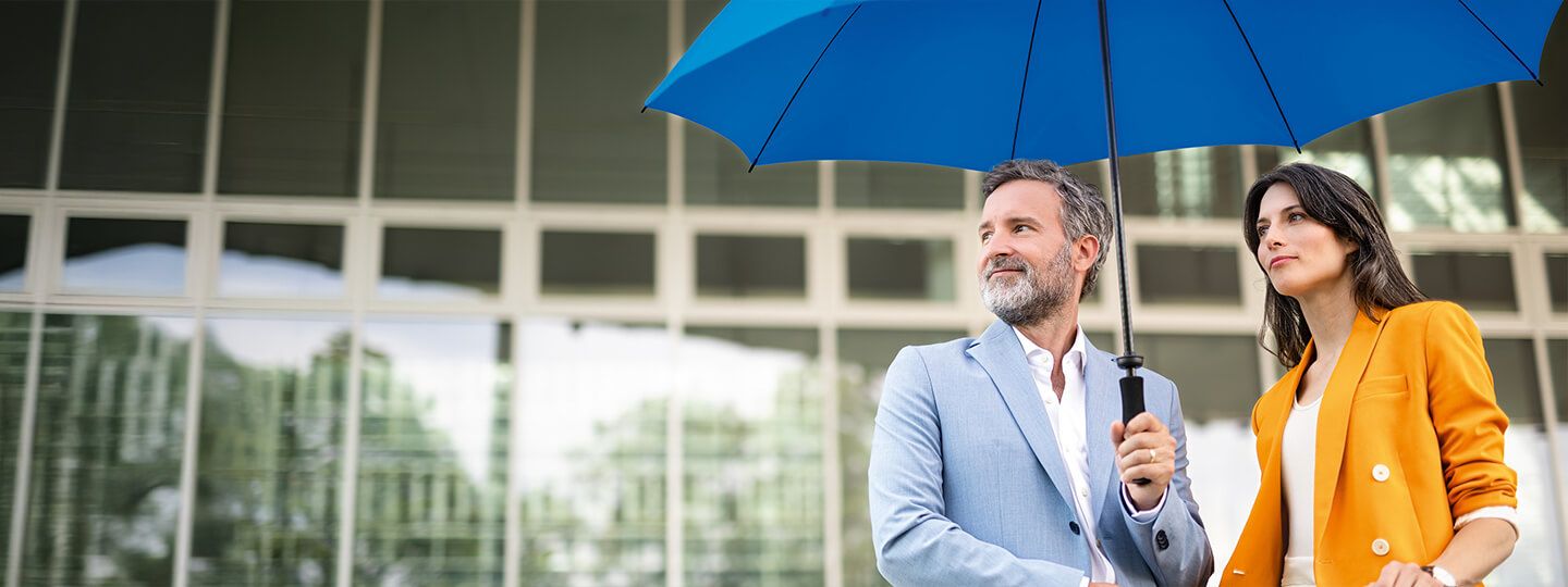 Ein Mann und eine Frau in Businesskleidung unter einem blauen Schirm 