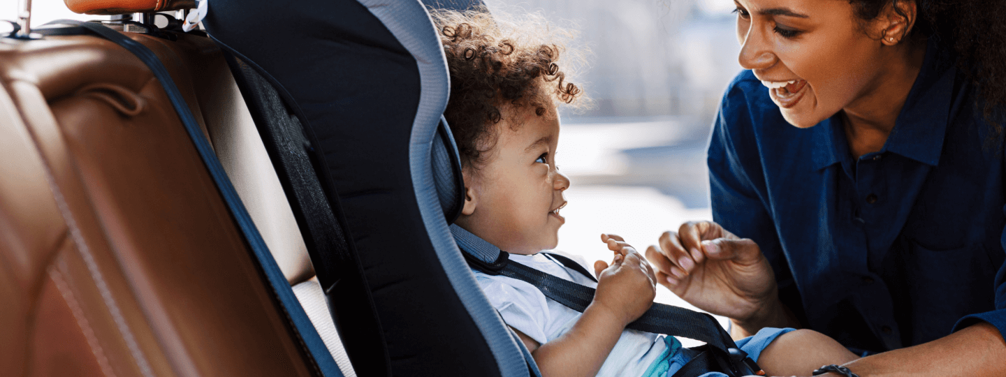Eine Mutter lacht ihren Sohn an, der im Auto im Kindersitzt sitzt.
