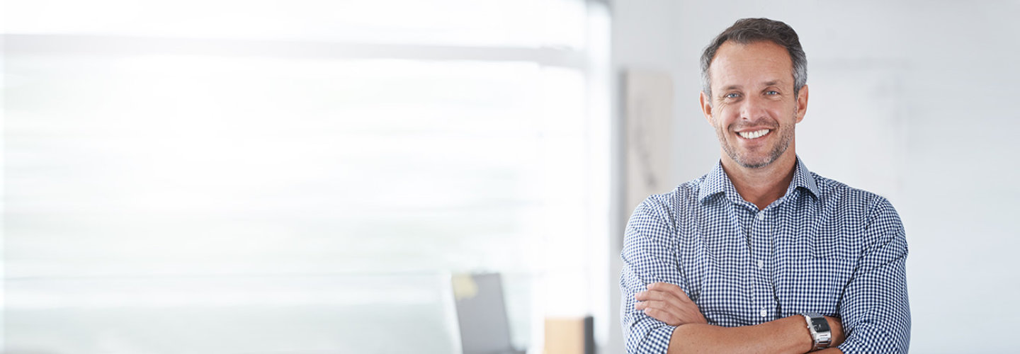 Unternehmer steht lächelnd mit verschränkten Armen in seinem Büro