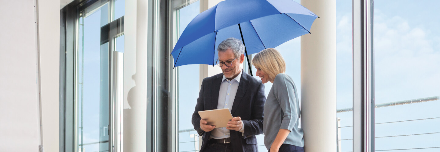 Frau und Mann schauen in einem Raum unter einem blauen Schirm auf ein Tablet