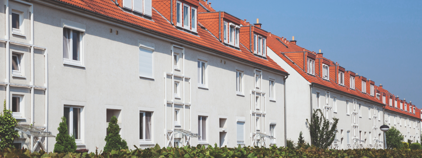 Mann steht gedankenversunken vor Mehrfamilienwohnhaus
