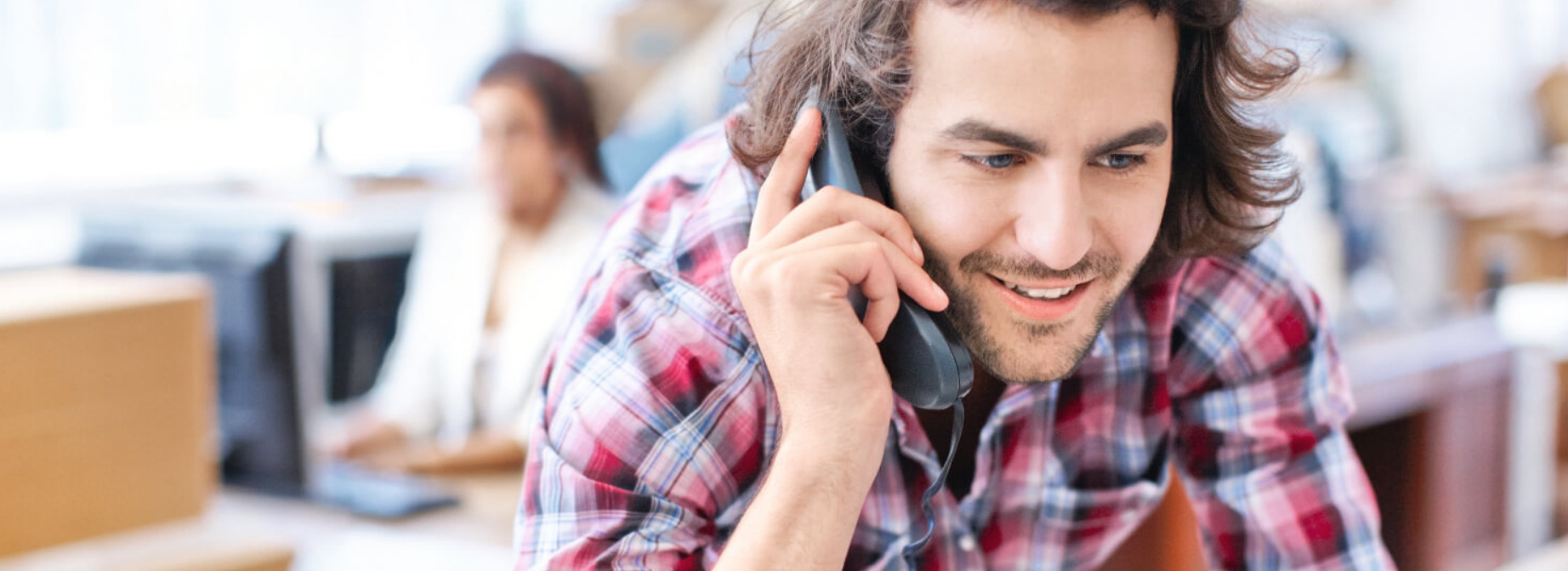Mann im Caro-Hemd telefoniert an seinem Schreibtisch