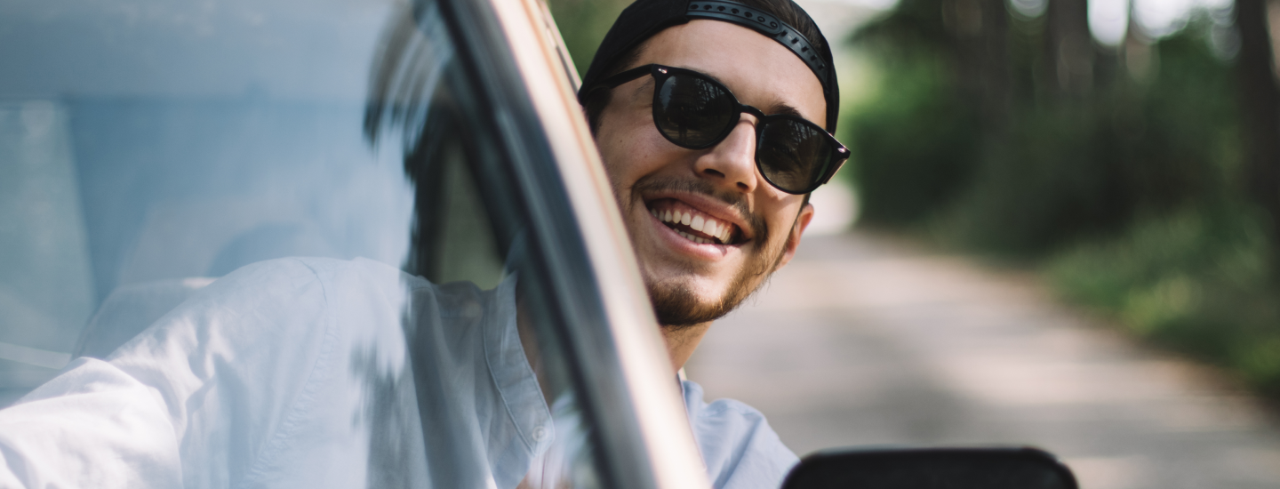 Lachender Mann lehnt sich aus dem Autofenster.