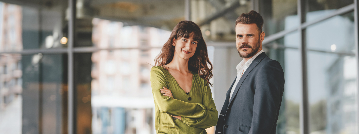 Junge Frau mit verschränkten Armen und junger Mann vor Glasfassade