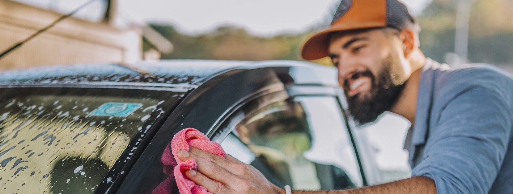 Lächelnder Mann putzt sein Auto.