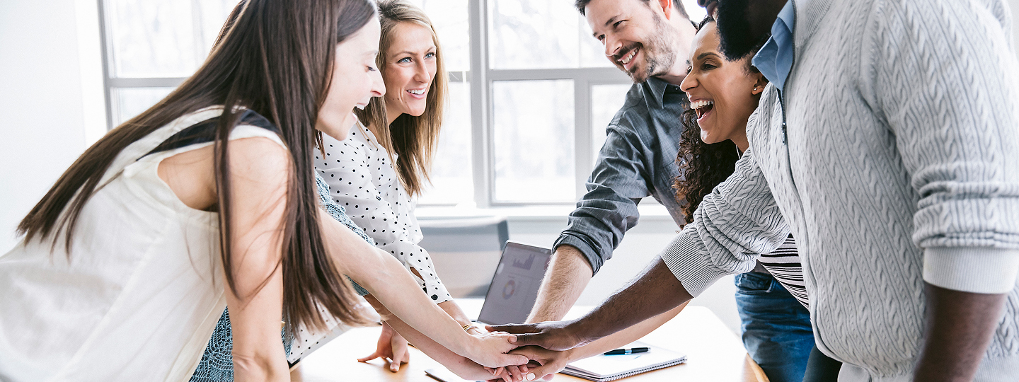 Diverses Team schlägt miteinander über einem Schreibtisch die Hände ein