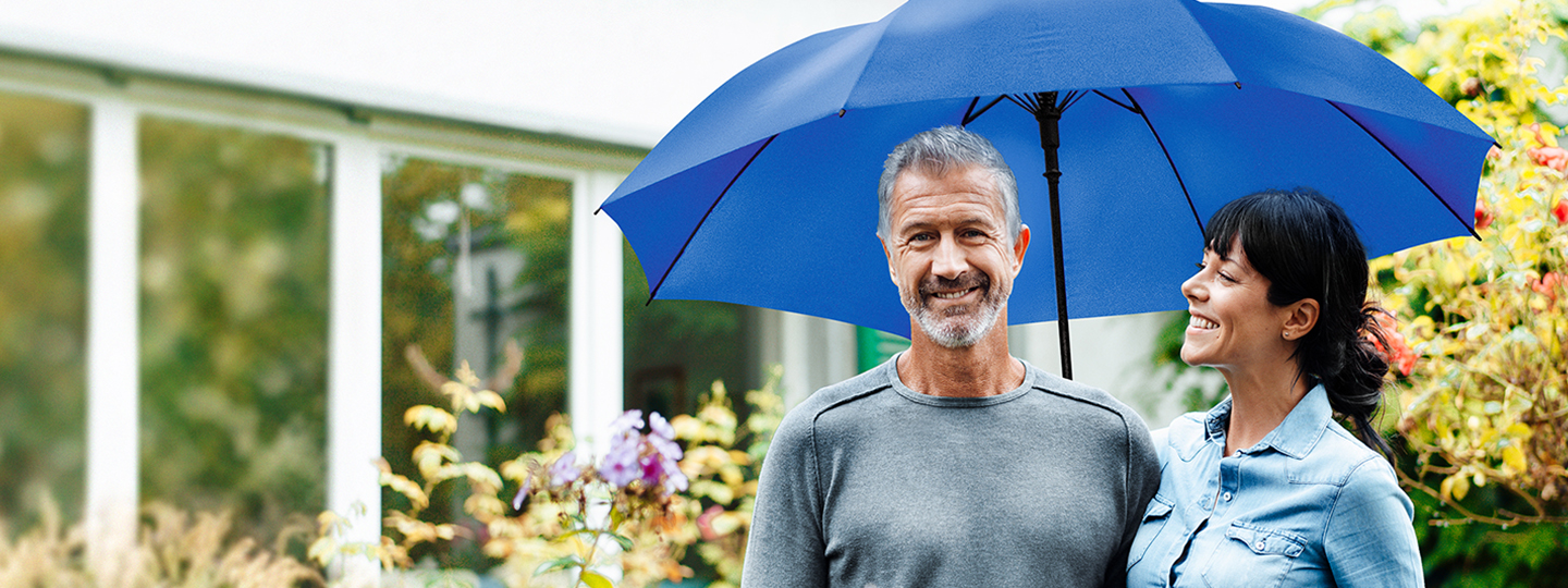 Mann und Fraue stehen in einem Garten unter einem blauen Regenschirm