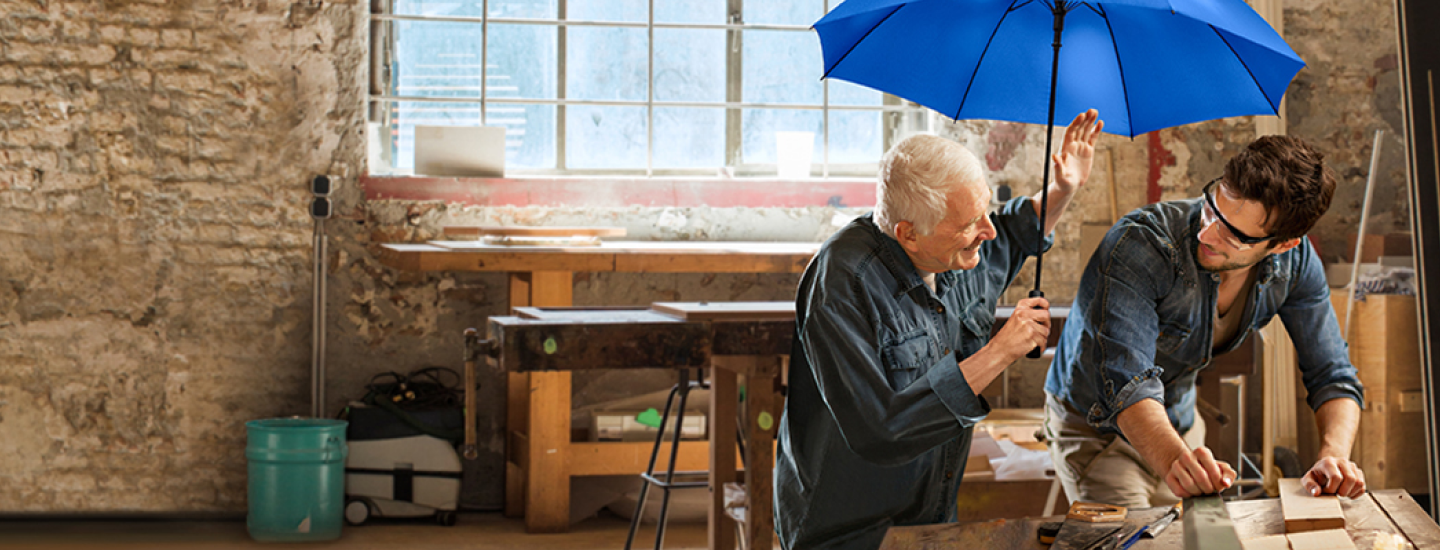 Ein jüngerer und ein älterer Handwerker sitzen unter dem blauen Schutzschirm.