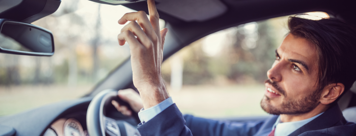 Mann sitzt am Steuer und drückt im Auto einen Knopf.