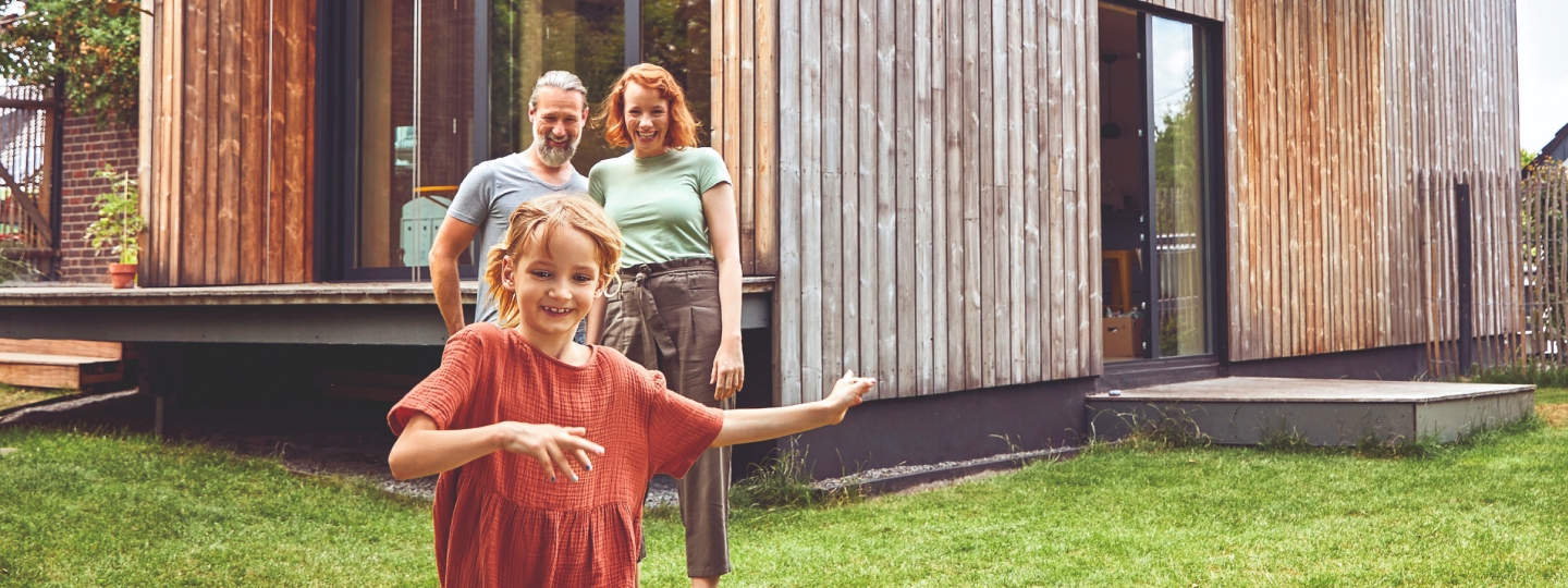 Ein sich umarmendes Ehepaar steht im Garten vor seinem Haus.
