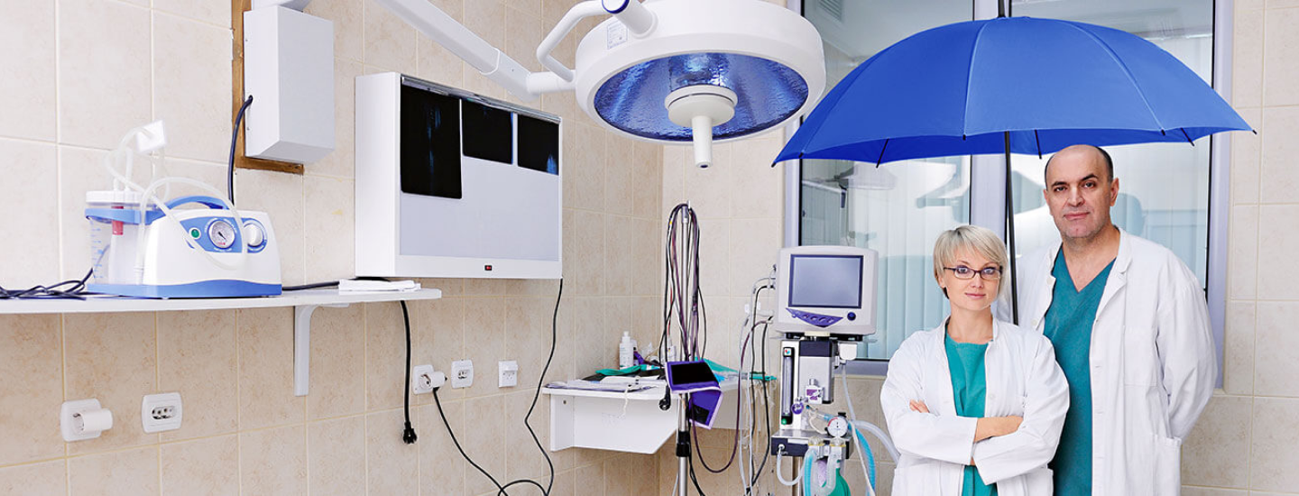 Mann und Frau aus dem Gesundheitsbereich im Behandlungszimmer unter dem blauen Schutzschirm