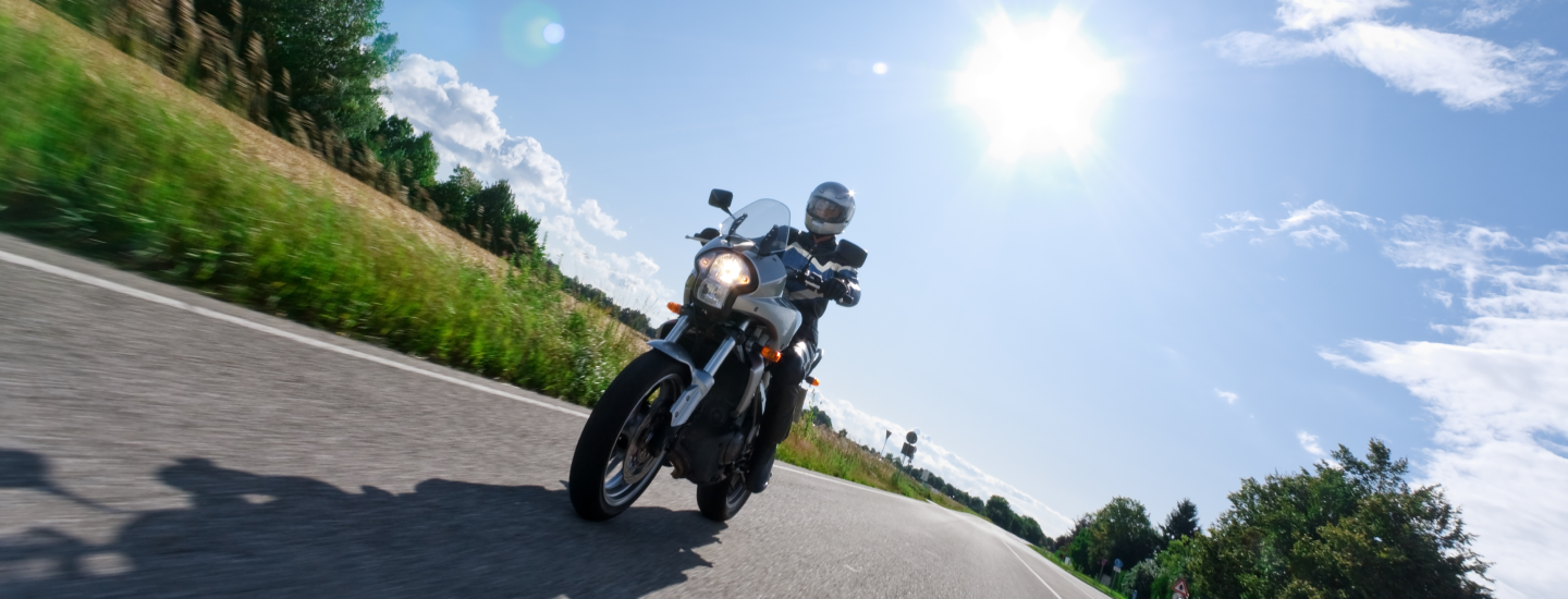 Motorradfahrer auf Landstraße bei Sonnenschein
