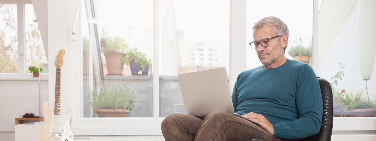 älterer Mann sitzt in Sessel und schaut in Laptop