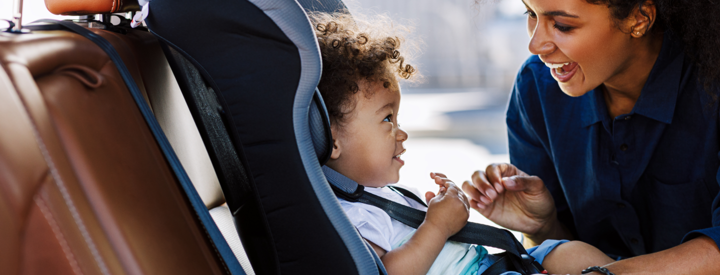 Eine Mutter lacht ihren Sohn an, der im Auto im Kindersitzt sitzt.