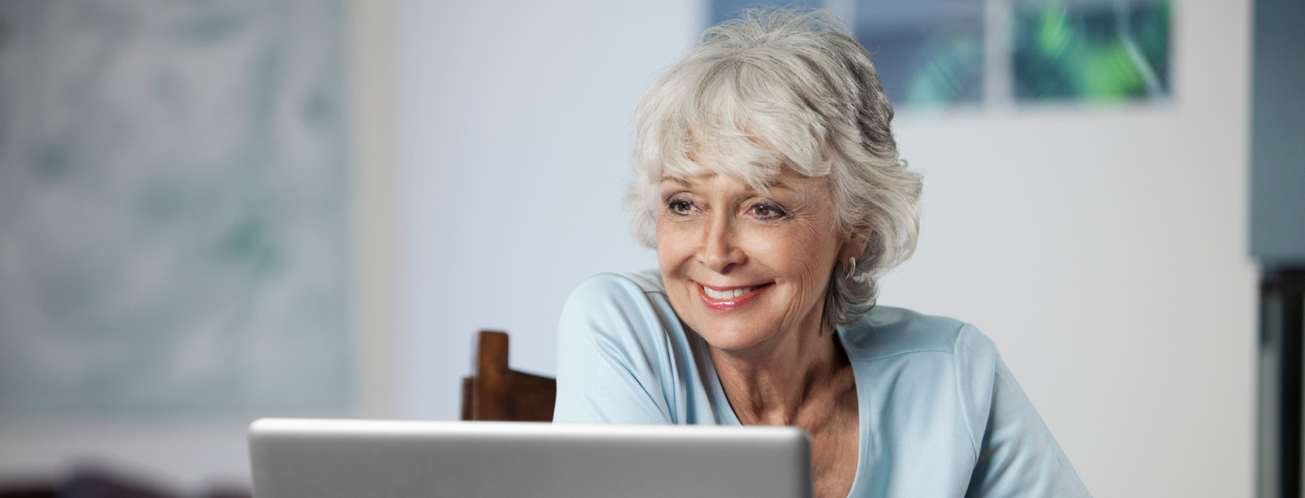 Dame mit grauen Haaren schaut auf Laptop und lächelt