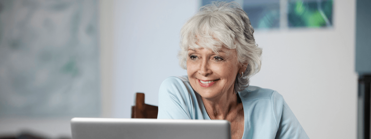 Dame mit grauen Haaren schaut auf Laptop und lächelt