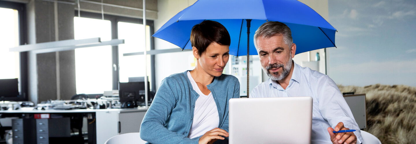 Frau und Mann schauen in einem Büro unter einem blauen Schirm auf einen Laptop