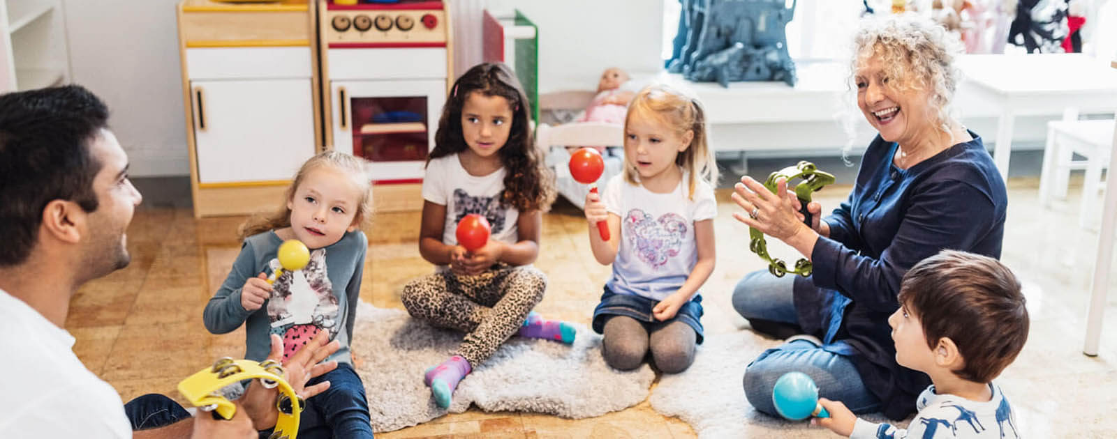 Erzieher sitzen mit Kindern und Rasseln im Sitzkreis