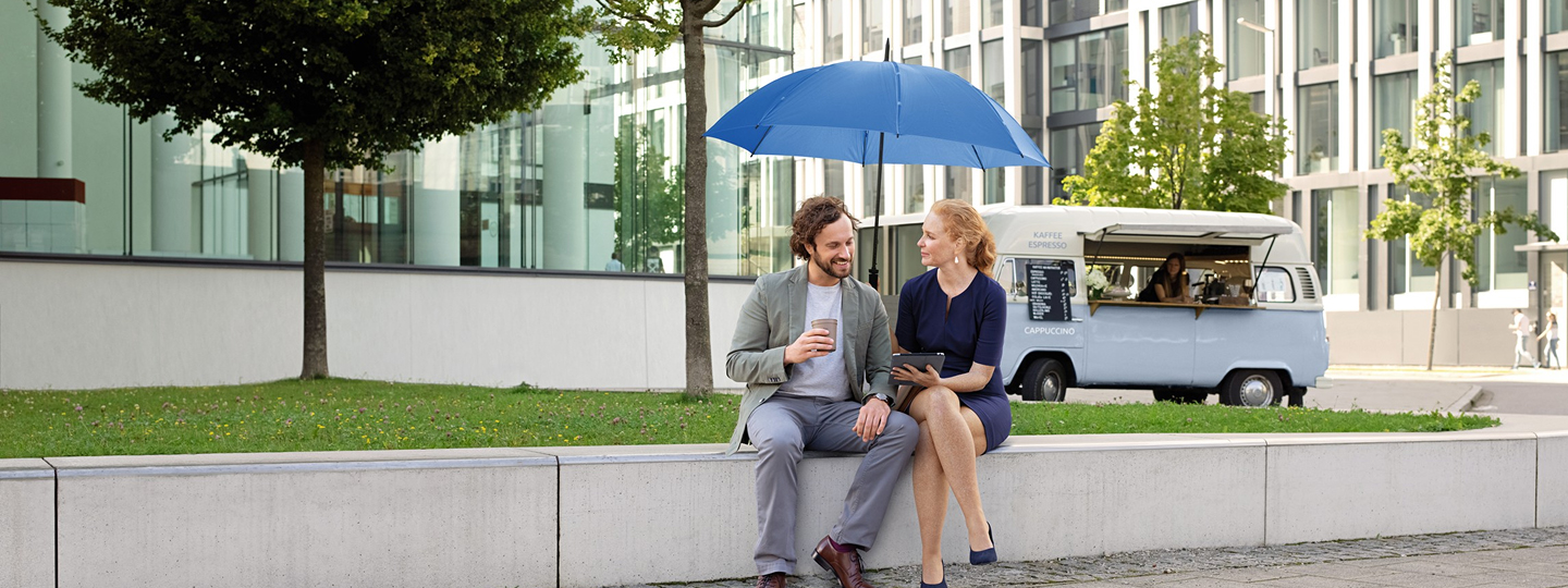 Ein Mann und eine Frau sitzen auf einer Steinmauer unter einem blauen Schutzschirm