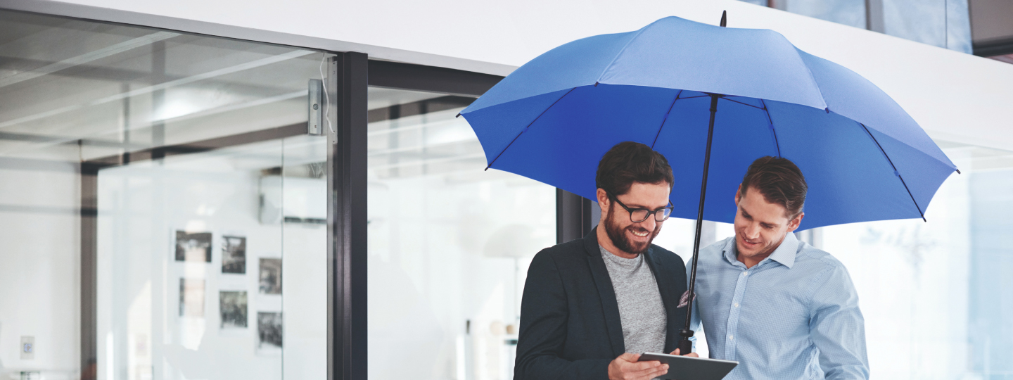 Zwei Männer unter dem blauen Schutzschirm schauen sich etwas auf Tablet an