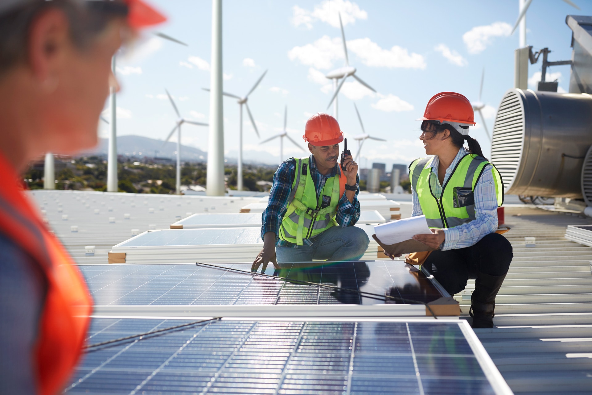Drei technische Mitarbeiter mit Schutzhelmen vor einer Kulisse von Wind- und Solarenergieanlagen