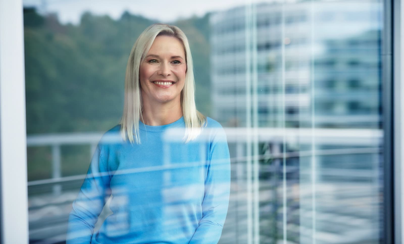 Eine Person steht hinter einem Fenster, lächelt und schaut nach draußen.