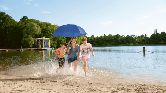 Frau mit blauem Schirm und zwei Kindern fröhlich am Strand